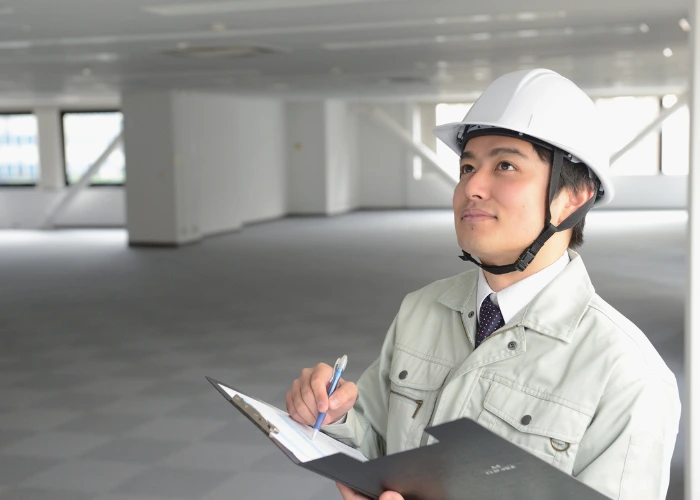 A man wearing a hard hat and white shirt stands with a clipboard, focused on conducting ADA inspections.